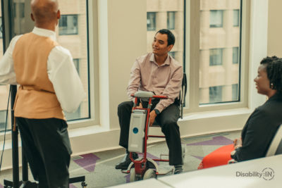 Three people in a meeting while one presents. One person is on a motorized scooter.