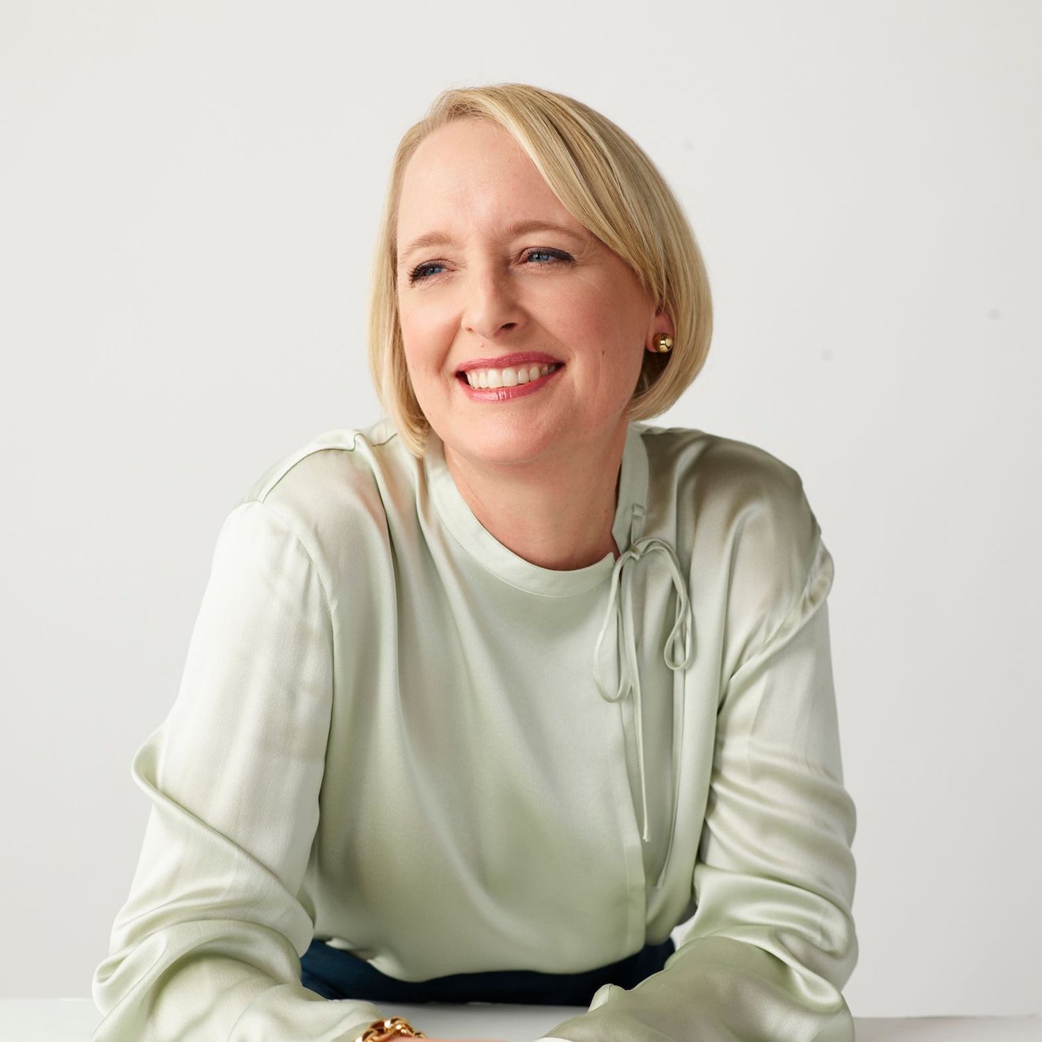 White woman with short blonde hair wears light grey silk top and smiles