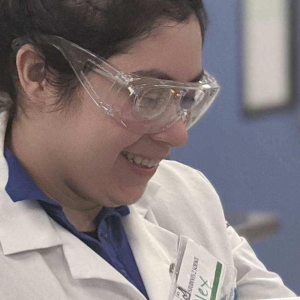 Woman smiling in lab coat and goggles.