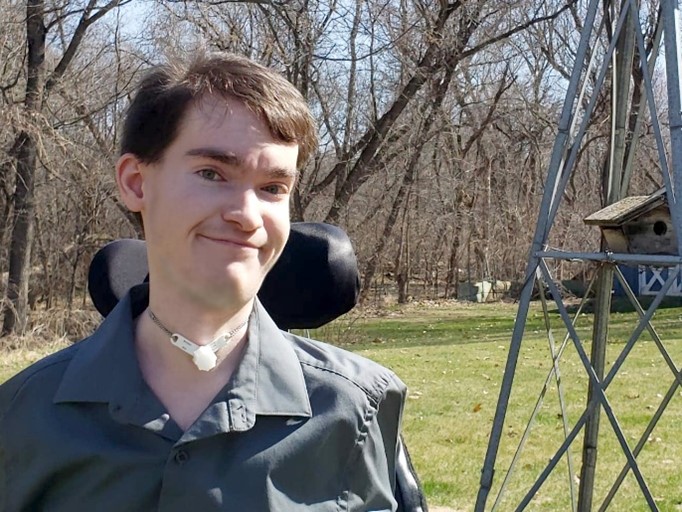 Photo of Ethan, a white man smiling, with neck support and tracheostomy tube.