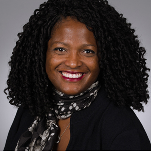 Black woman with curly black hair wears a black top and patterned scarf and smiles