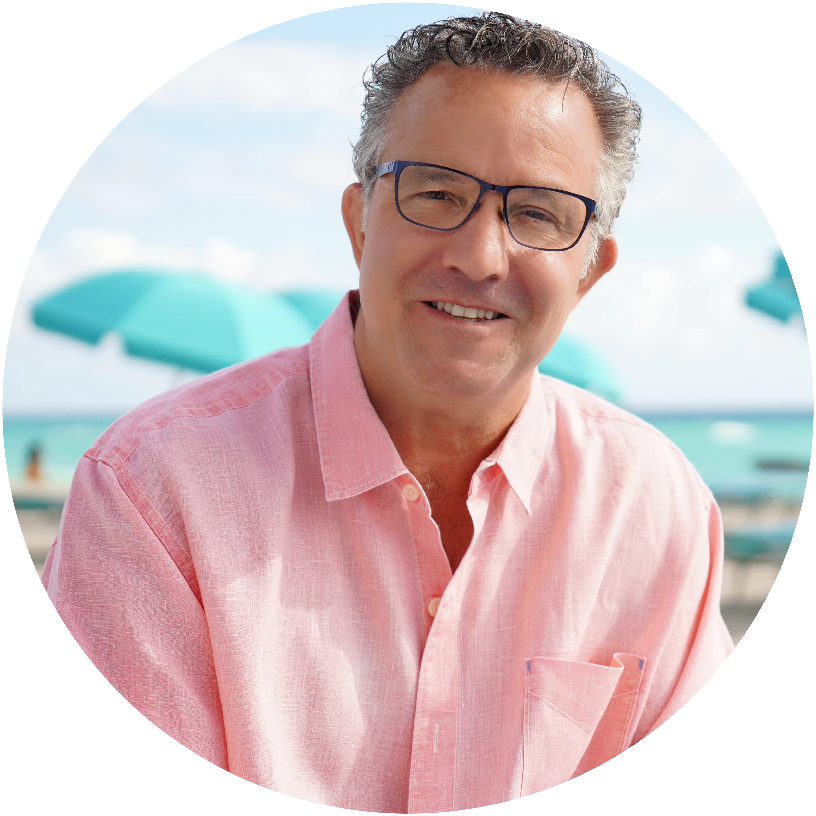 Andrew Houghton, a white male with short grey hair and glasses wears a pink collared shirt against a beach background.