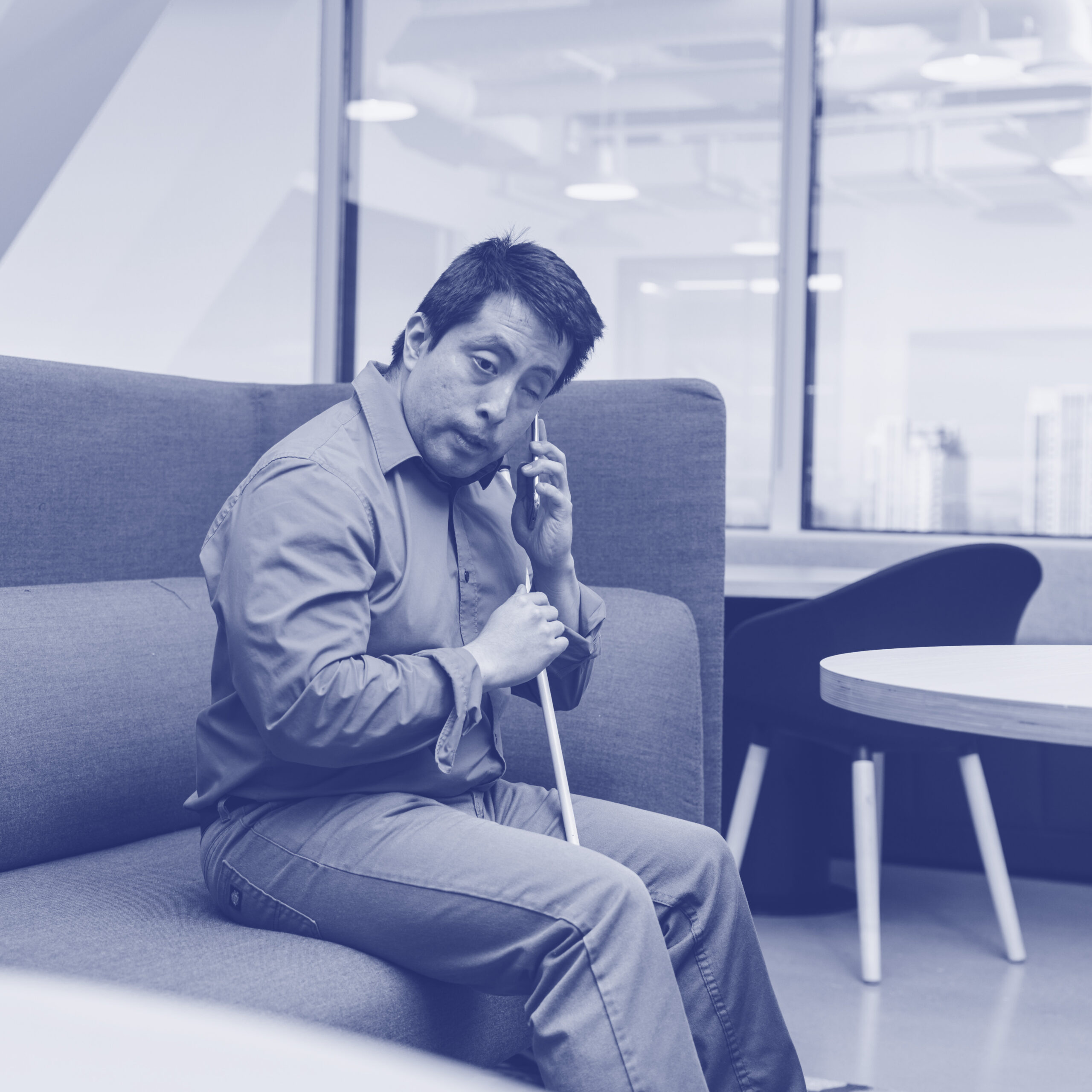 Israel, a Blind man, listens to his phone at a corporate office booth.