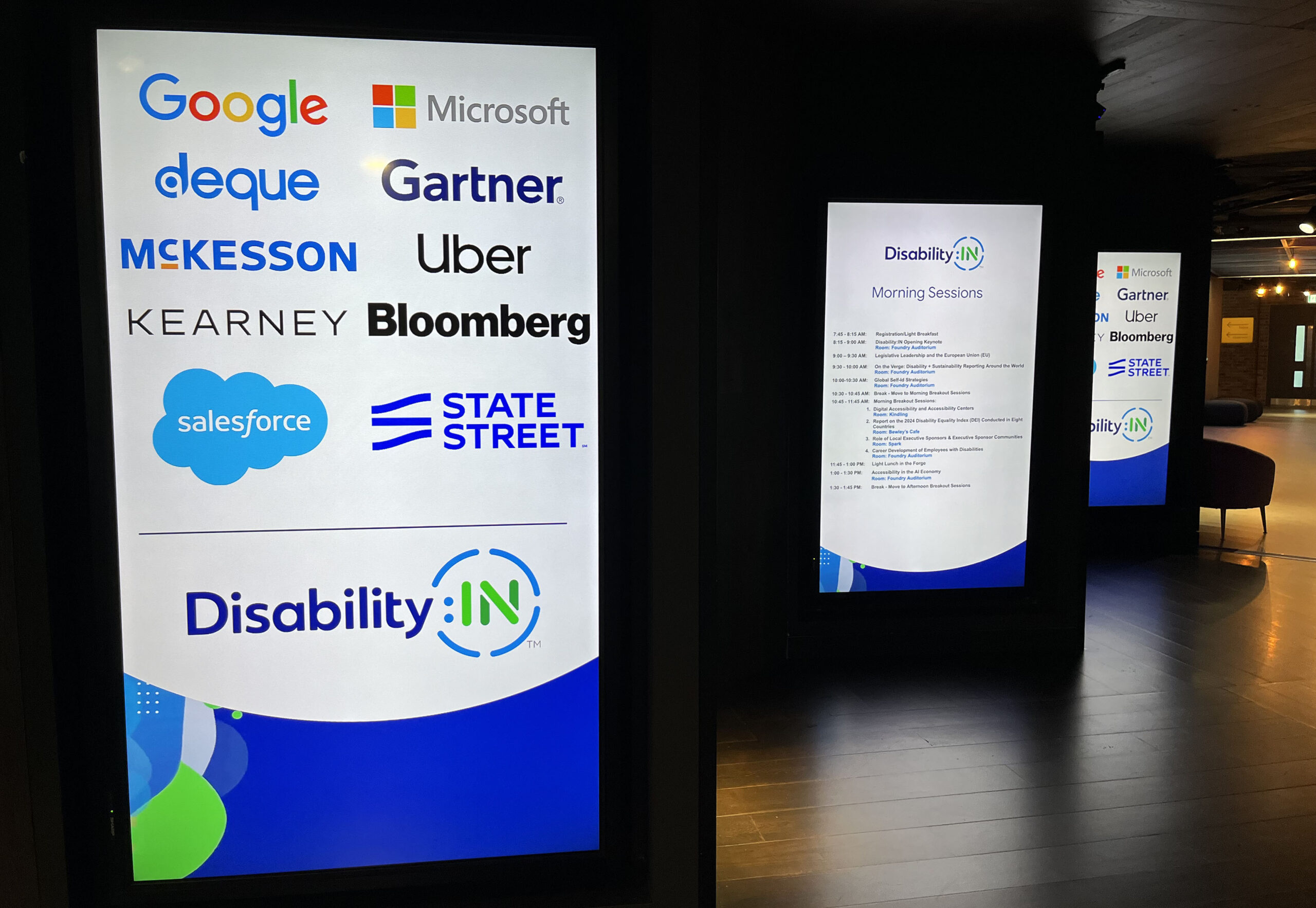 Illuminated signage with partners: Google, Microsoft, Deque, Gartner, McKesson Uber, Kearney, Bloomberg, Salesforce, State Street. Disability:IN is featured with blue and green circle designs.