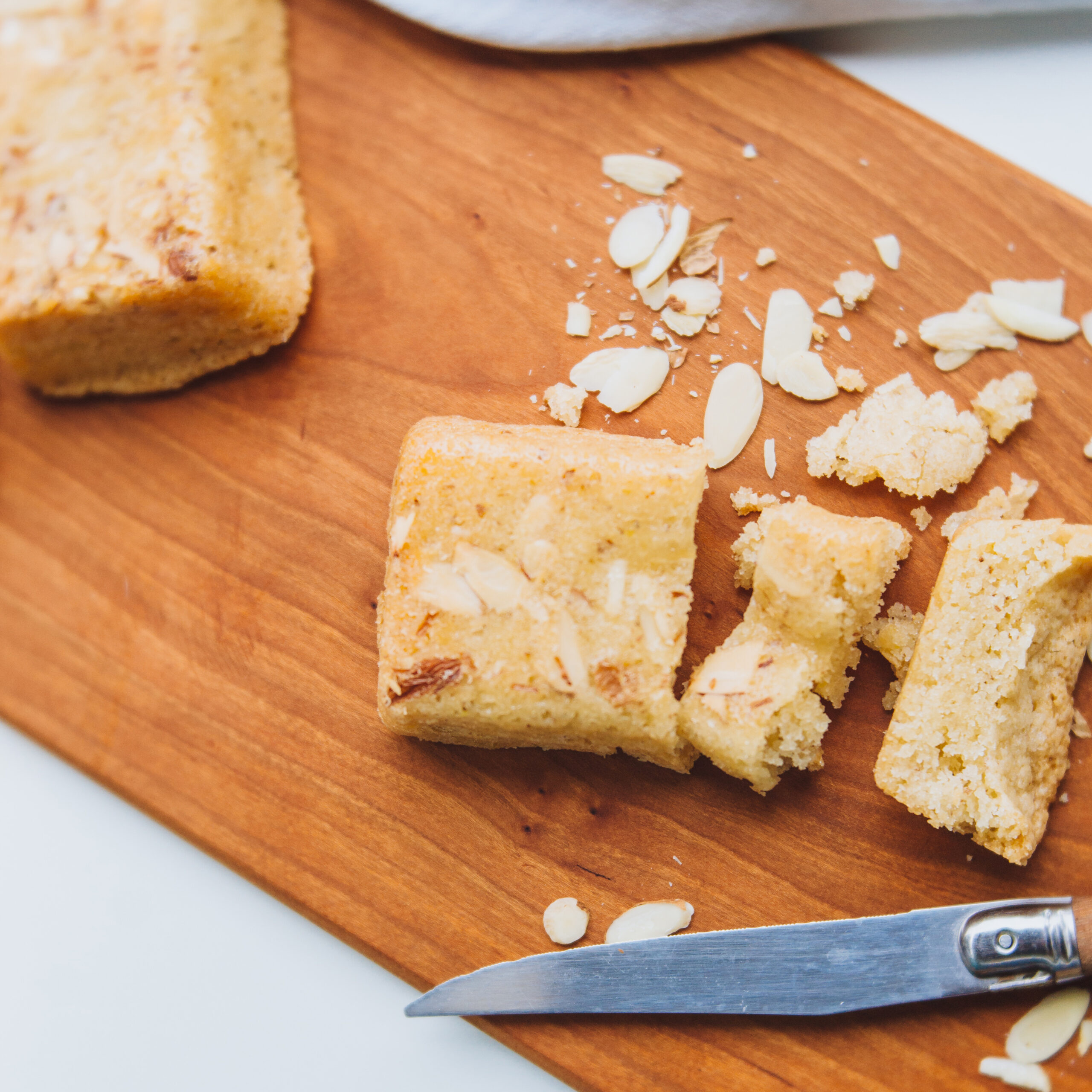 Carina's Bakery Scandinavian Almond Cake shown on a wooden cutting board, sliced up.