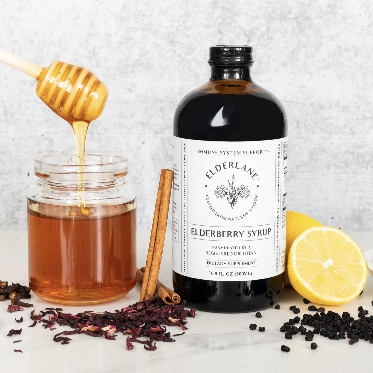 Elderlane Elderberry syrup in dark bottle, pictured with honey jar and lemon.