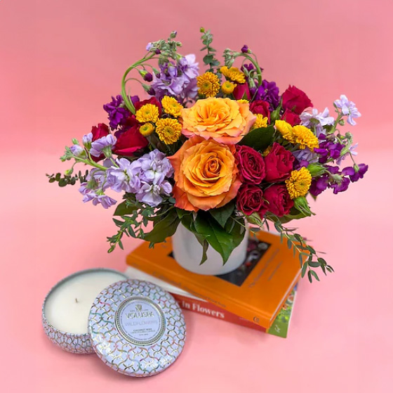 Colorful flower arrangement in yellows, reds, purples, with decorations against a pink background.