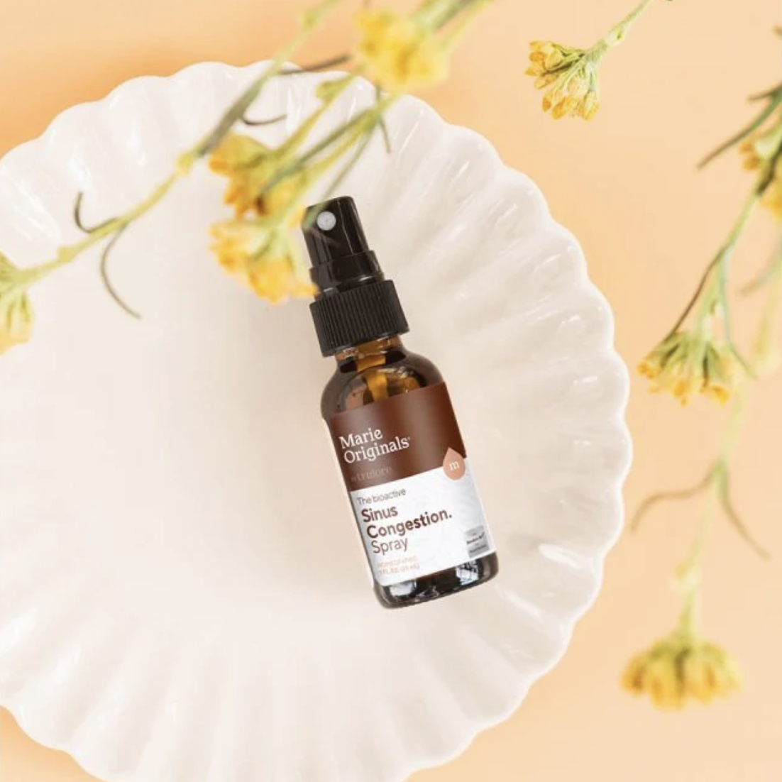 Marie Originals Sinus Relief Spray. Brown amber glass bottle shown on top of a scalloped plate with flowers.